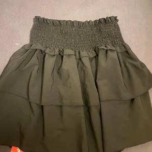 Svart kjol från Romwe - Snygg svart kjol från Romwe med elastisk midja som ger en bekväm passform. Kjolen är kort och har en volangdetalj som ger extra stil. Perfekt för att skapa en trendig look.