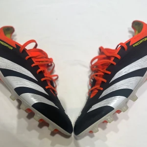 Adidas Predator elite fotbollsskor  - Snygga Adidas Predator fotbollsskor i svart med vita och orange detaljer. Skorna har en modern design med snörning och en slitstark sula för optimalt grepp på planen. Om du har funderingar på priset, kontakta mig och vi kan diskutera 