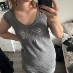 Grå stickad klänning - mysig grå stickad med korta ärmar och ett fint hålmönster vid bysten i form av en fjäril. (Katt och kanin finns i hemmet)