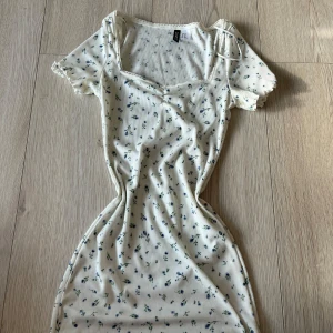 Vit blommig klänning från Divided - Söt vit klänning från Divided med blå blommor och ribbad struktur. Den har korta ärmar och en fin v-ringad hals. Perfekt för en somrig look! 🌸