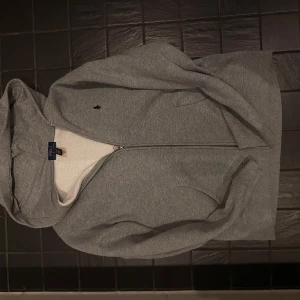 Grå hoodie från Polo Ralph Lauren - Säljer en stilren grå hoodie från Polo Ralph Lauren med dragkedja och det klassiska logotypbroderiet på bröstet. Tröjan har en mjuk insida och är perfekt för kyliga dagar. Hör av dig vid intresse! 😊