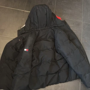 Svart pufferjacka från Tommy Hilfiger - Säljer en svart barn pufferjacka från Tommy Hilfiger. I storlek 164. Säljer eftersom att jag växt ut den för längesen.