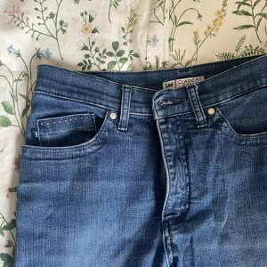 Blå jeans från Lee med rhinestones  - Snygga blå jeans från Lee i klassisk passform. De har dekorativa rhinestones på fickorna och en rak benform. Perfekta för en avslappnad stil. Köpta för 600 kr men kommer inte till användning.