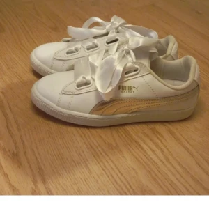 Vita sneakers T sommarn - Snygga vita Puma sneakers med breda satinband som snörning och gulddetaljer på sidan. Perfekta för en stilren look med en touch av glamour.