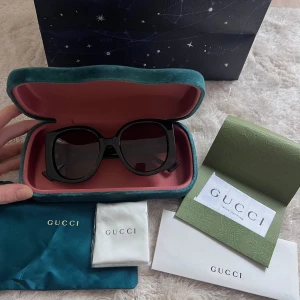 Svart/Bruna  solglasögon från Gucci - Snygga svarta solglasögon från Gucci med breda skalmar och guldiga logodetaljer. Glasögonen har en fyrkantig form och kommer i ett elegant fodral. Kvitto, cerifikat, påse & oanvänd duk att putsa dem med.