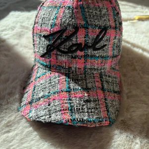 Rutig keps från Karl Lagerfeld - Trendig keps från Karl Lagerfeld med ett färgglatt rutigt mönster i grått, rosa och blått. Kepsen har en broderad logga framtill och är perfekt för att ge din outfit en färgklick.
