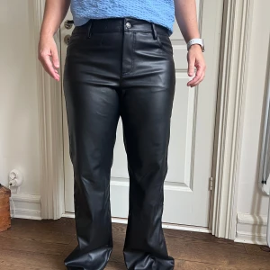 Svarta skinnbyxor - Snygga svarta skinnbyxor med hög midja och raka ben. Byxorna har en stilren design med knappar och dragkedja framtill.  Använda 1 ggr. Strl 42