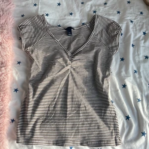 Randig topp från H&M - Säljer en randig topp från H&M i brunt och vitt. Toppen har en v-ringad design med korta ärmar och ett lätt rynkat parti framtill. Perfekt för en avslappnad stil.
