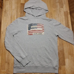 Grå hoodie från Ralph Laurens Denim&supply - Grym hoodie från Ralph Laurens Denim&supply, med vintageinspirerad amerikansk flagga. Stl M. Finfint skick, inga defekter! ✨Fråga gärna mått etc. 