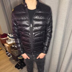 Svart Moncler Acorus - Tja! Säljer denna snygga svarta pufferjacka från Moncler. Jackan har en glansig finish och är utrustad med dragkedja framtill. Väldigt fint skick förutom ett hål längst ned vid vänster ärm, skriv privat för bilder på skadan. Den har en hög krage och Moncler-loggan på ärmen. Perfekt för kyligare dagar, Givetvis äkta! Vid minsta fundering är det endast att höra av sig!
