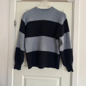 Randig stickad tröja i mörkblå och blå - Säljer en mysig stickad tröja med breda ränder i blått och grått. Tröjan har en normal passform och långa ärmar, perfekt för kyligare dagar. Den är enkel och stilren, vilket gör den lätt att matcha med olika outfits.