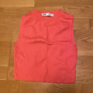 Korallfärgad ribbad linnetopp från Zara - Säljer en snygg korallfärgad ribbad linnetopp från Zara. Perfekt för varma dagar med sin ärmlösa design och mjuka material. Enkelt att matcha med olika outfits för en stilren look.