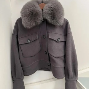 Grå meotine kappa - Snygg grå meotine kappa med en lyxig pälsdetalj på kragen. Jackan har knappar framtill och två stora fickor med lock på bröstet. Perfekt för kyligare dagar när du vill hålla stilen. 
