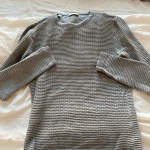 Grå stickad tröja från Selected Homme - Säljer en stilren grå stickad tröja från Selected Homme. Tröjan har ett diskret randigt mönster och långa ärmar. Perfekt för kyligare dagar och ger en klassisk look.