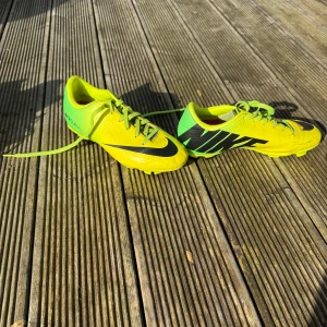 Gula fotbollsskor från Nike gräskor - Säljer ett par gula fotbollsskor från Nike med svarta detaljer och snörning. Skorna har en sportig design och är perfekta för fotbollsplanen.