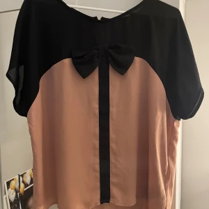 Svart och beige topp med rosett  - Säljer en snygg topp från Forever 21 i svart och beige. Toppen har en söt rosett på framsidan och korta ärmar. Storlek L 