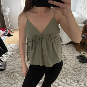 Olivgrön linnetopp med knytband - Säljer en olivgrön linnetopp från zara med smala axelband och v-ringning. Toppen har knytband på sidorna.