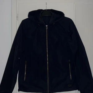 Svart jacka från Dondup - Snygg svart jacka från Dondup med dragkedja framtill och huva. Jackan har två praktiska fickor med dragkedjor och en stilren design. Perfekt för en cool och avslappnad look.