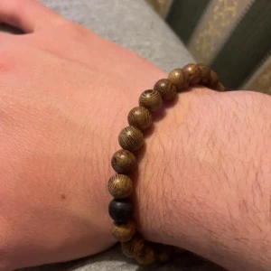 Brunt armband med träpärlor - Snyggt armband med bruna träpärlor och en svart pärla som accent. Perfekt för en naturlig och stilren look. Elastiskt band för enkel passform. 