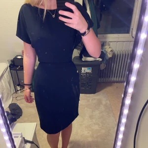 Svart klänning med knytband - Snygg svart/mörkblå klänning med knytband i midjan och korta ärmar. Perfekt för en stilren look. Klänningen har en slits baktill för extra rörelsefrihet. 