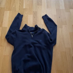 Mörkblå tröja från Ralph Lauren - Säljer en stilren mörkblå tröja från Ralph Lauren med dragkedja vid halsen. Tröjan har långa ärmar och är tillverkad i bomull, vilket gör den både bekväm och snygg. Perfekt för kyligare dagar. Pris går justera