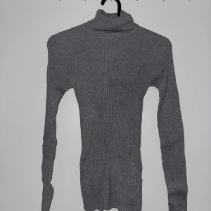 Grå ribbad polotröja från Gina Tricot - Aldrig använd! Säljer en stilren grå ribbad polotröja från Gina Tricot. Tröjan har en tight passform och långa ärmar, perfekt för kyligare dagar. Den höga kragen ger en extra touch av elegans. Passar utmärkt till både jeans och kjol. 🖤