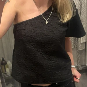 Svart oneshoulder topp från Vila - Snygg one shoulder topp från vila med ett diskret skimrande blommönster! Ändas använd en gång 🤩