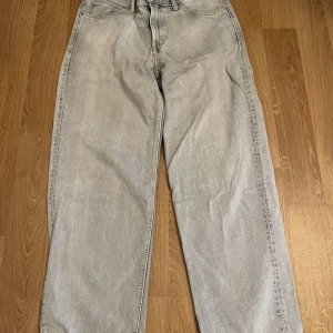 Grå loose fit jeans - Säljer ett par grå loose fit jeans med klassisk femficksdesign. Byxorna har en avslappnad passform och är perfekta för en casual look. De är tillverkade i ett slitstarkt material och har en knappgylf.