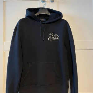 Ralph Lauren hoodie - Ralph lauren hoodie med snygg logga i svart. Hoodien är i bra skick förutom ett litet hål bak på luvan som är svårt att märka vid användning. Hör av er om ni har några frågor eller funderingar!