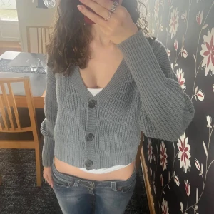 Grå stickad kofta - Säljer en mysig blågrå stickad kofta med knappar framtill. Koftan är croppad och har långa ärmar, perfekt för en avslappnad stil. Passar bra till jeans eller kjol💛