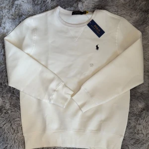 Vit tröja från Ralph Lauren - Säljer en stilren vit tröja från Ralph Lauren med det klassiska broderade logotypen på bröstet. Tröjan har långa ärmar och en rund halsringning. Perfekt för en avslappnad och snygg look.