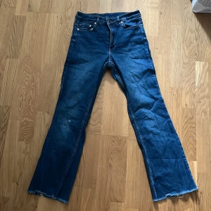 Blå bootcut jeans från H&M - Snygga blå bootcut jeans från H&M med hög midja. Perfekta för en avslappnad stil. Tillverkade i denim med klassisk femficksdesign och knappgylf. Ett litet slitage på vänster knä går att laga. Innebenslängden är 70,5 cm. Midjemått 34 cm.