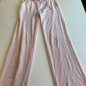 Rosa mjukisbyxor från Juicy Couture - Snygga rosa mjukisbyxor från Juicy Couture med glittrande stenar som bildar texten 'Juicy' på baksidan. Byxorna har en bekväm passform och är perfekta för en avslappnad stil.