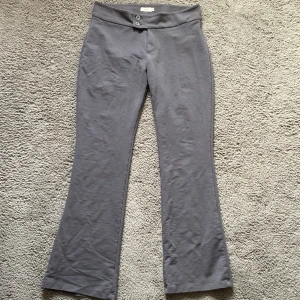 Grå byxor från Nelly - Snygga grå byxor från Nelly med låg midja och bootcut-stil. Byxorna har två knappar framtill och är tillverkade i ett mjukt material som ger en bekväm passform. Perfekta för en avslappnad look.