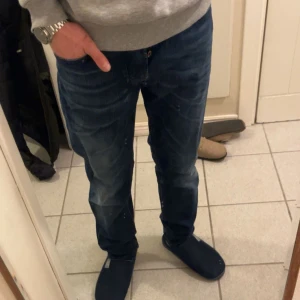 Blå jeans från Diesel - Snygga blå jeans från Diesel med en klassisk femficksdesign och subtila slitningar för en trendig look. De har en knappgylf och är perfekta för en avslappnad stil. Storlek 30/32