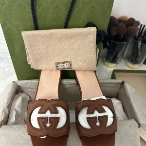 Bruna sandaler från Gucci - Snygga bruna sandaler från Gucci med det ikoniska GG-emblemet i fram. Perfekta för en stilren look. Sandalerna har en öppen design och är tillverkade i skinn.