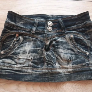 Jeanskjol - Snygg jeanskjol med slitna detaljer och dubbla knappar fram. Kjolen har fickor både fram och bak samt dekorativa sömmar. Perfekt för en avslappnad stil.