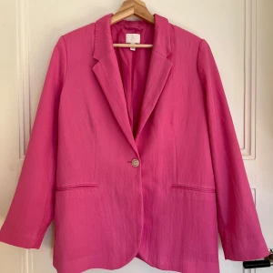 Rosa kavaj från H&M - Snygg rosa kavaj från H&M med en enkel knapp framtill. Den har en klassisk krage och långa ärmar, perfekt för att liva upp din outfit. Kavajen har en stilren design med två fickor framtill.