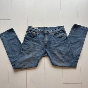 Levis 502 jeans - Snygga Levis 502 jeans i en klassisk blå färg. Dessa jeans har en straight passform och är tillverkade i slitstarkt denim. Perfekta för en avslappnad stil med fem fickor och knappgylf. Liten fläck längste ner på byxbenet 