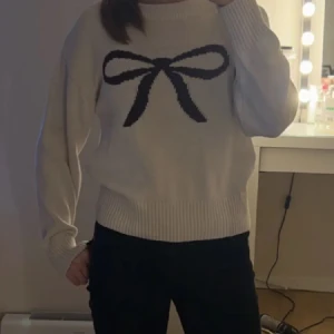 Vit stickad tröja med rosettmotiv - LÅNAD BILD! Säljer en söt vit stickad tröja med en stor mörk rosett på bröstet. Tröjan har rund hals, ribbade muddar och långärmad passform. Perfekt för dig som gillar gulliga detaljer och vill ha en mysig look. Postar alltid samma dag som köp 🩷Pris kan diskuteras 💐 storlek 170