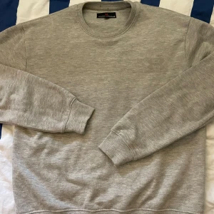 Grå sweatshirt från Under Armour - Säljer en stilren grå sweatshirt från Under Armour i storlek M. Tröjan har rund hals, ribbade muddar och ett diskret Under Armour-logotryck på bröstet. Perfekt för chill dagar eller när du vill ha en enkel look. Materialet är mjukt och känns skönt mot huden.