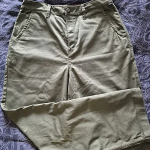 Olivgröna chinos från Vans, stl 30 - Snygga olivgröna chinos från Vans med klassisk rak passform. Byxorna har sidfickor, bakficka med knapp och bälteshällor. Materialet är mjuk bomull som känns skönt mot huden. Perfekt för dig som gillar streetwear och vill ha en clean look.