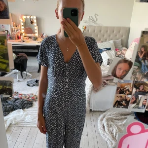 Blå blommig byxdress från & Other Stories - Supersöt blå byxdress från & Other Stories med vitt blommigt mönster. Byxdress har korta ärmar, v-ringning och knappar framtill. Den är figurnära upptill och har en mjuk, flowy känsla. Perfekt för dig som gillar en chill och feminin stil.