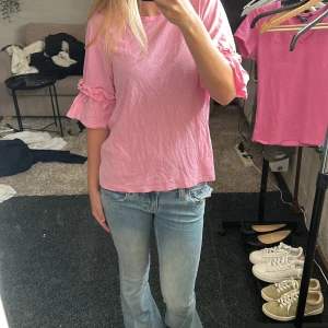 Rosa blus med volangärmar - Söt rosa blus från H&M med rund hals och korta ärmar som har volangdetaljer och rynk vid ärmslutet. Blusen är i mjuk bomull och har en loose passform som ger en chill vibe. Perfekt att styla med jeans eller kjol för en färgglad look. Tröjan har två små hål längst ner (kolla på sista bilden) men inget som märks när den är på! 