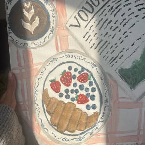 Paris Coffee - En konstnärlig tavla med motiv av en fransk frukost: croissant, bär, kaffe och en Vogue-tidning. Perfekt för dig som älskar caféer, Paris och estetik! Inspirerar till kreativa stunder och drömmar om storstadsliv men den är även signerad av Savannah Jensen . Storlek: 42x33