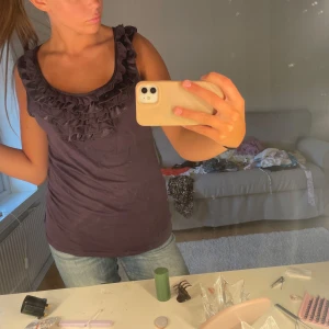 Mörklila linnetopp med volang - Säljer en mörklila linnetopp med breda axelband och snygga volangdetaljer runt halsringningen. Toppen är ärmlös och har en figurnära passform som sitter snyggt. Perfekt att styla med jeans eller kjol för en chill look.