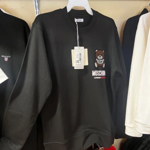 Svart Moschino sweatshirt med björn - Svart sweatshirt från Moschino med broderad nallebjörn och logotypen 'MOSCHINO UNDERBEAR' på bröstet. Tröjan har rund hals, långa ärmar och är tillverkad i 100% bomull. Perfekt för dig som gillar streetwear och vill sticka ut med en ikonisk design.