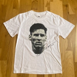 Vit t-shirt med grafiskt tryck - Vit t-shirt i bomull med ett stort grafiskt tryck på framsidan som föreställer ett ansikte och en signatur. Klassisk rund hals och korta ärmar. Perfekt för dig som gillar stilrena plagg med en cool twist.