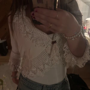 Vit kofta med spetsdetaljer - Superfin vit kofta med breda spetsdetaljer och virkad look. Perfekt att styla över linne eller klänning för en extra touch. Från Vintage Stories i storlek 40/42. 100% Bomull