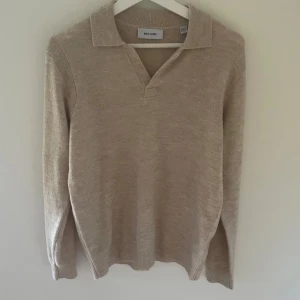 Beige stickad polotröja Only & Sons - Beige stickad polotröja från Only & Sons i mjukt material. Tröjan har klassisk krage med v-ringning och långa ärmar. Perfekt för lager-på-lager och enkel att matcha med jeans eller chinos.